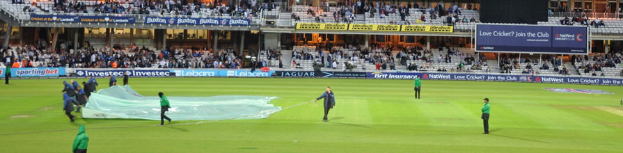 Oval staff pull the covers over a cricket pitch during a rain interrupted match.