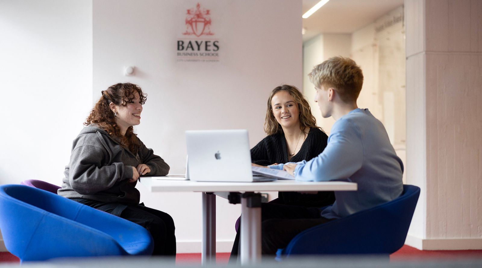 Three Bayes students sitting at a table with a laptop.
