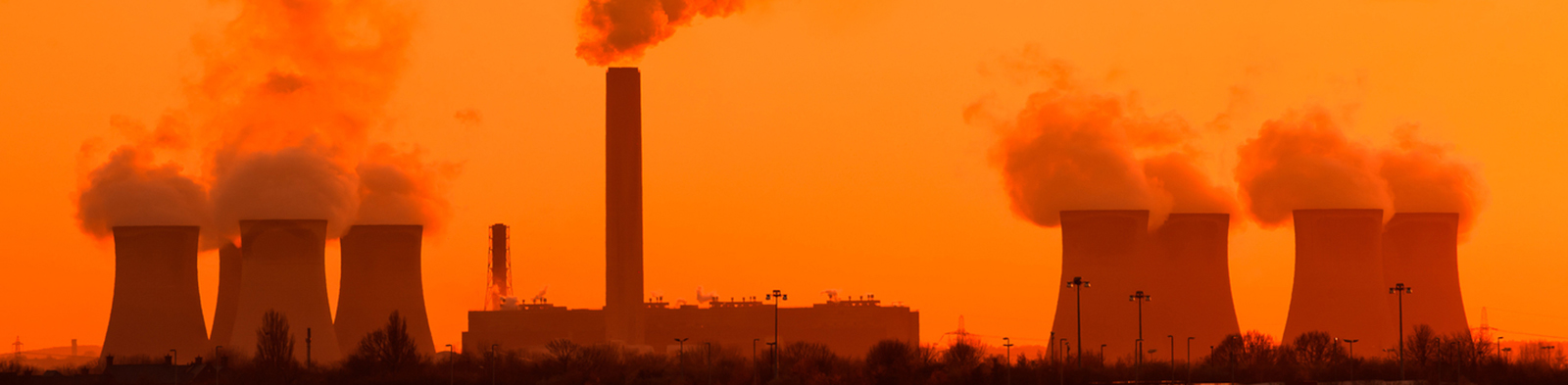 Coal station cooling towers with smoke coming out the chimney into orange sky