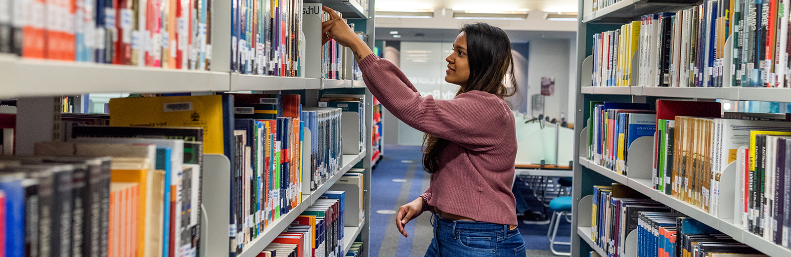 Female student placing a book back in the shelves in the library at Bayes 