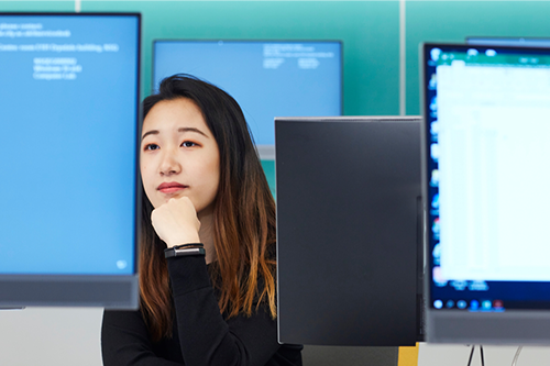 Photo of a girl sitting with computers around her thinking.