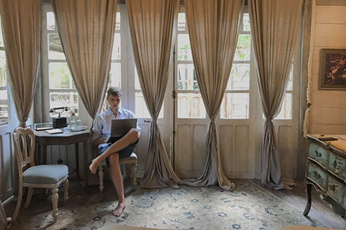 Nikita Kozachenko working on a laptop at home in a white shirt and chino shorts
