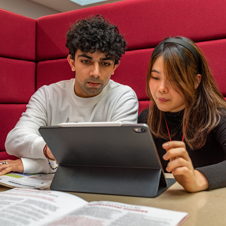 A young man and woman collaborating on a project together looking at a tablet in a study area.