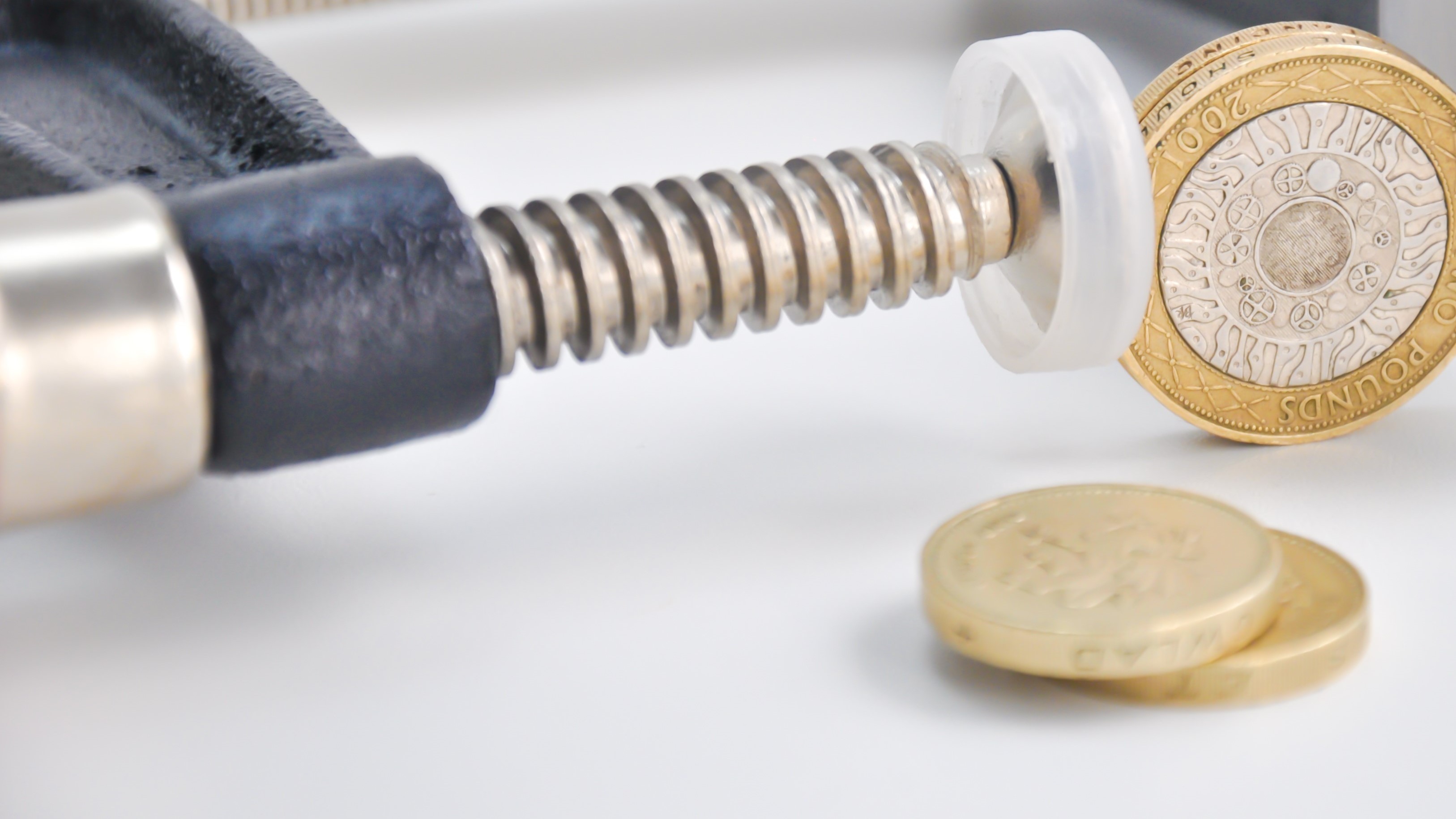 A pound coin is squeezed between a clamp