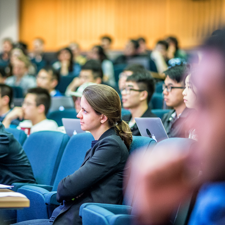 Students sitting in a tiered lecture hall, listening to a lecture on financial markets