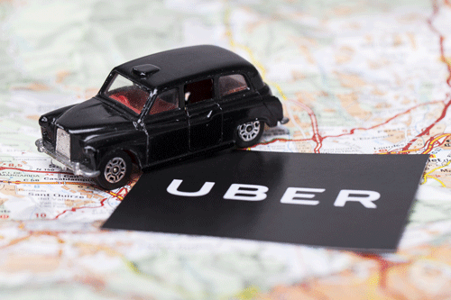Black taxi toy next to Uber logo on a map