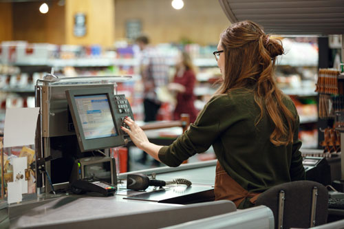 A woman sits at a cash register in a supermarket.