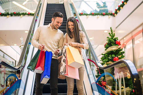 Man and woman walk down an escalator with shopping bags at Christmas