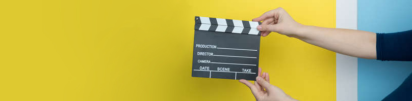 Female hands holding a film clapperboard on yellow and blue background