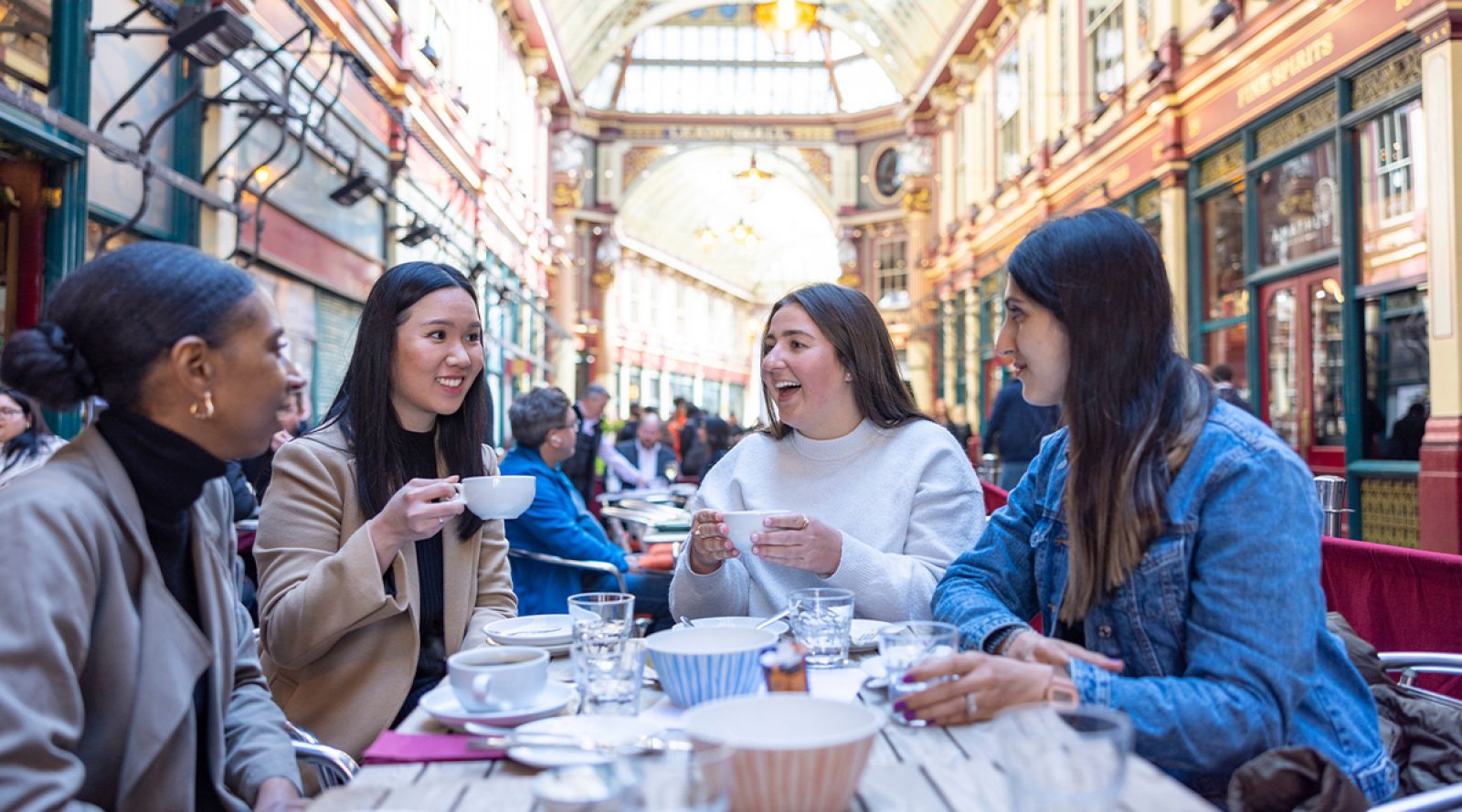 A group of women sitting at a table inside Leadenhall Market enjoying a cup of tea.
