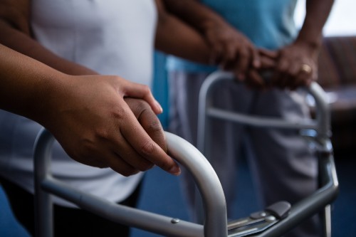 Cropped hands of nurse assisting woman in walking with walker at retirement home