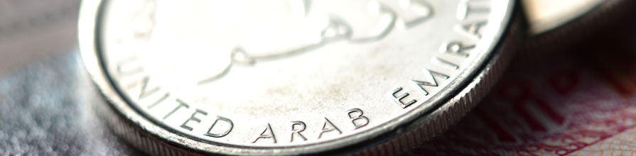An extreme close up of a one dirham UAE coin atop a nondescript UAE banknote.