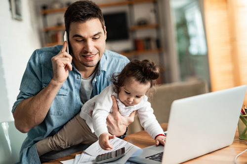 Man holding daughter while working on laptop